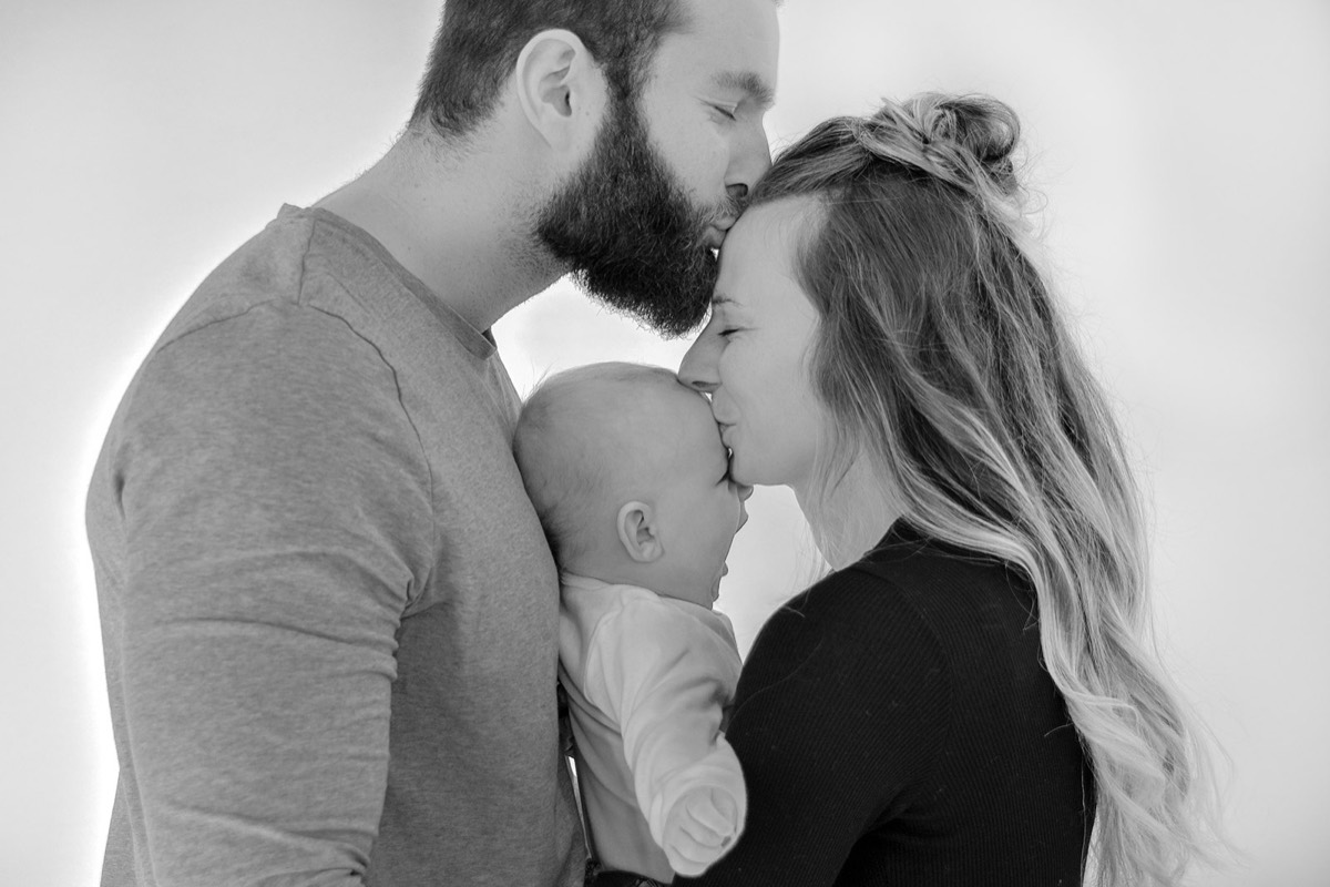 Schwarzweiß: Eltern küssen ihr Neugeborenes — Familienfotografie Berlin